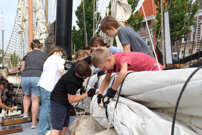 Jugendliche packen ein Großsegel eines Seleschiffs ein